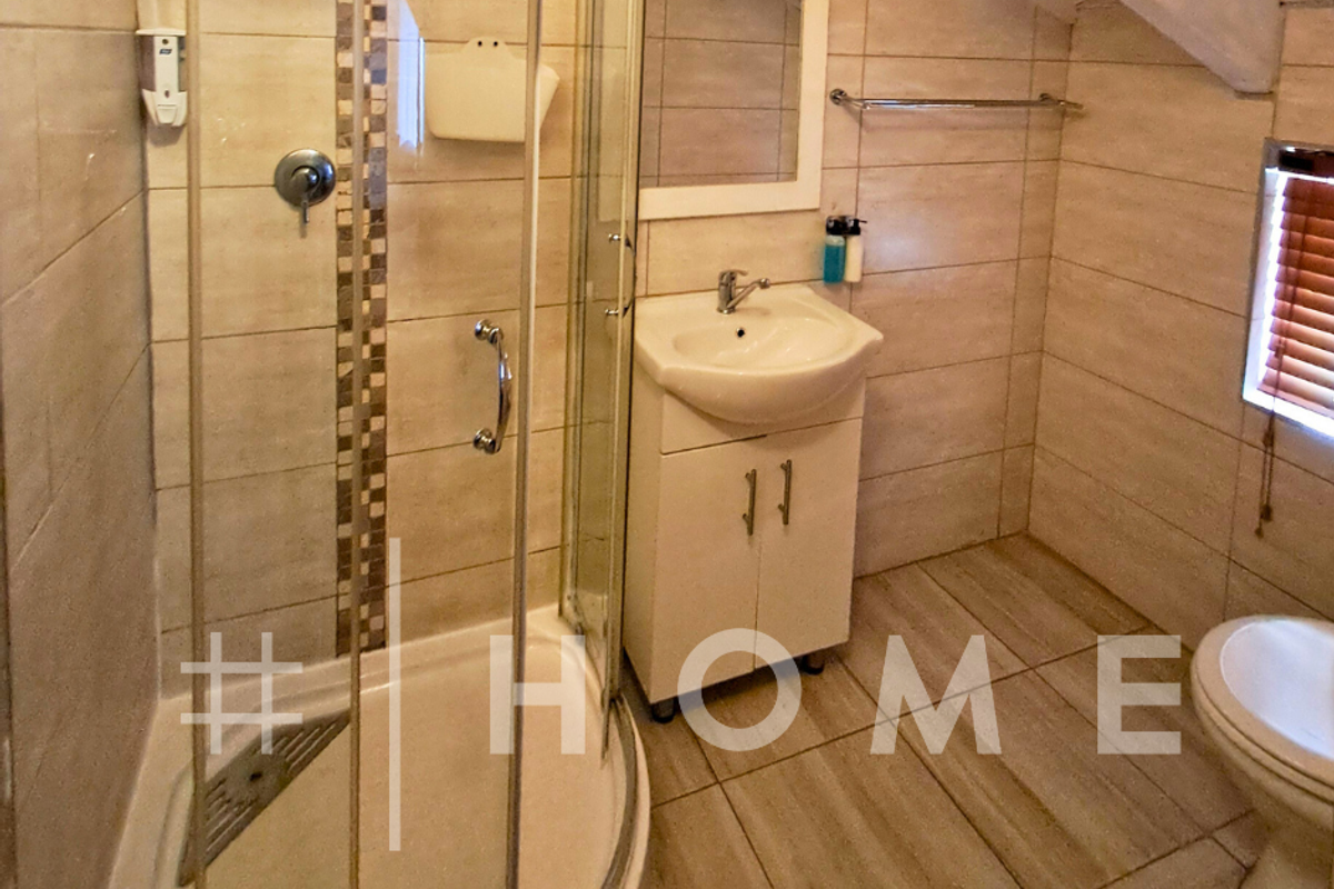 A compact bathroom featuring a corner shower enclosure, a vanity basin, a toilet, and tiled finishes under a sloped ceiling.