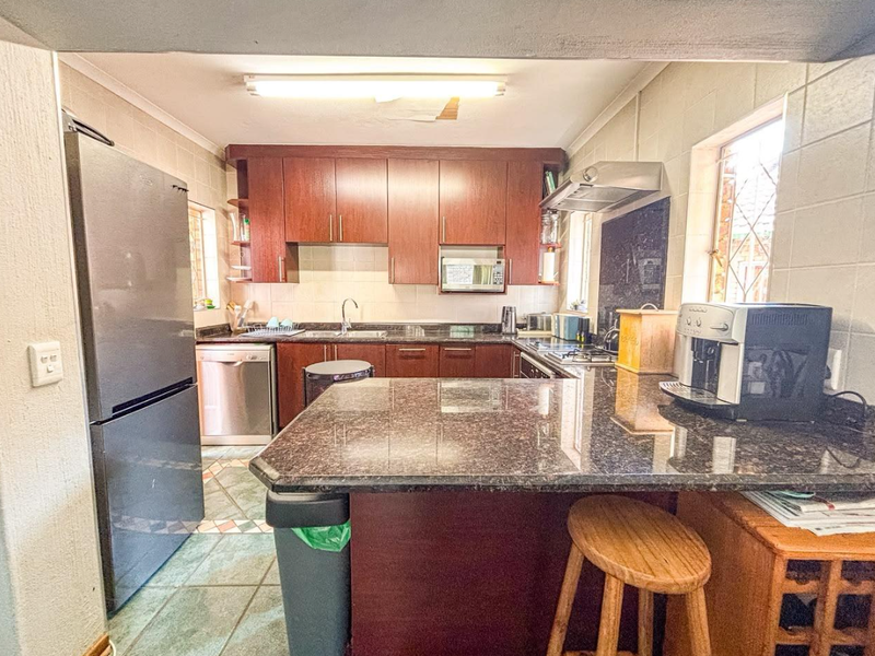 A functional kitchen featuring dark wood cabinetry, granite countertops, and a tiled backsplash, with a breakfast bar area and integrated appliances.