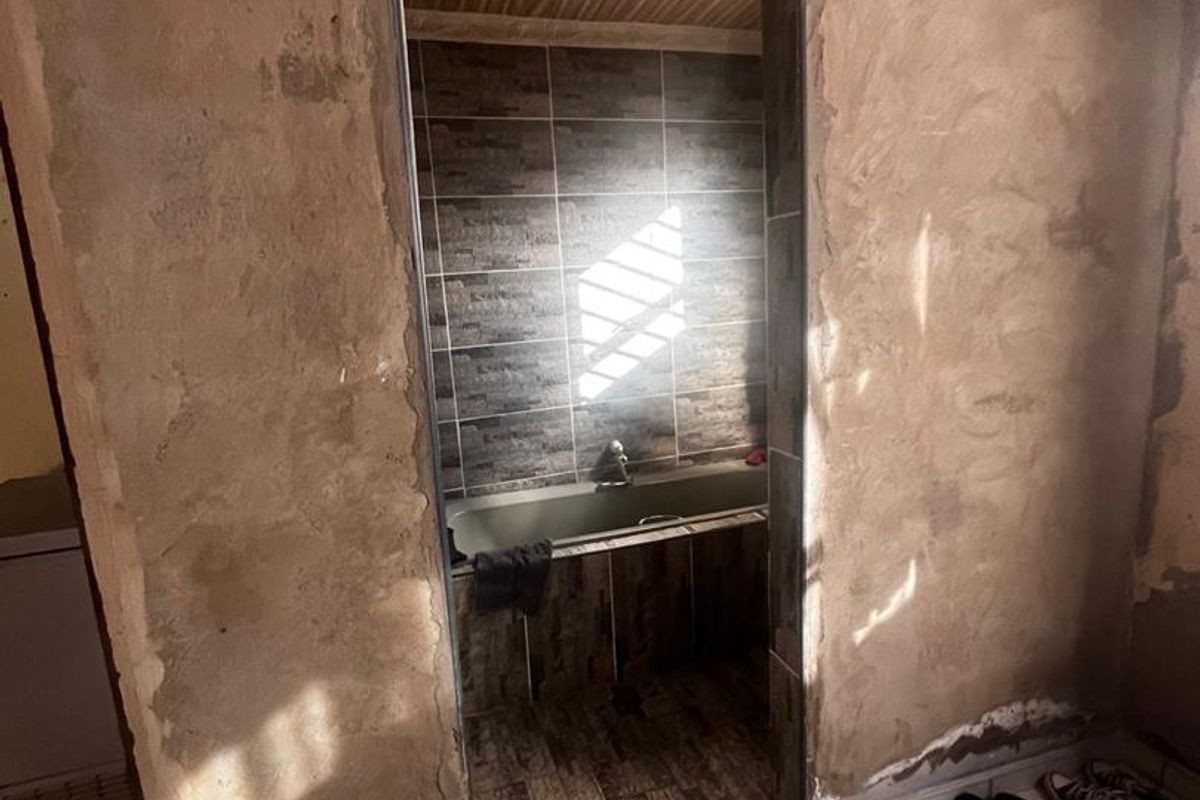 A bathroom interior featuring tiled walls and a bathtub, currently undergoing renovation with unfinished plasterwork on the surrounding walls.