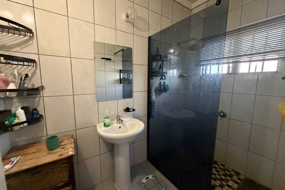 A functional bathroom featuring a pedestal basin, walk-in shower with a dark glass screen, and neutral wall tiling.