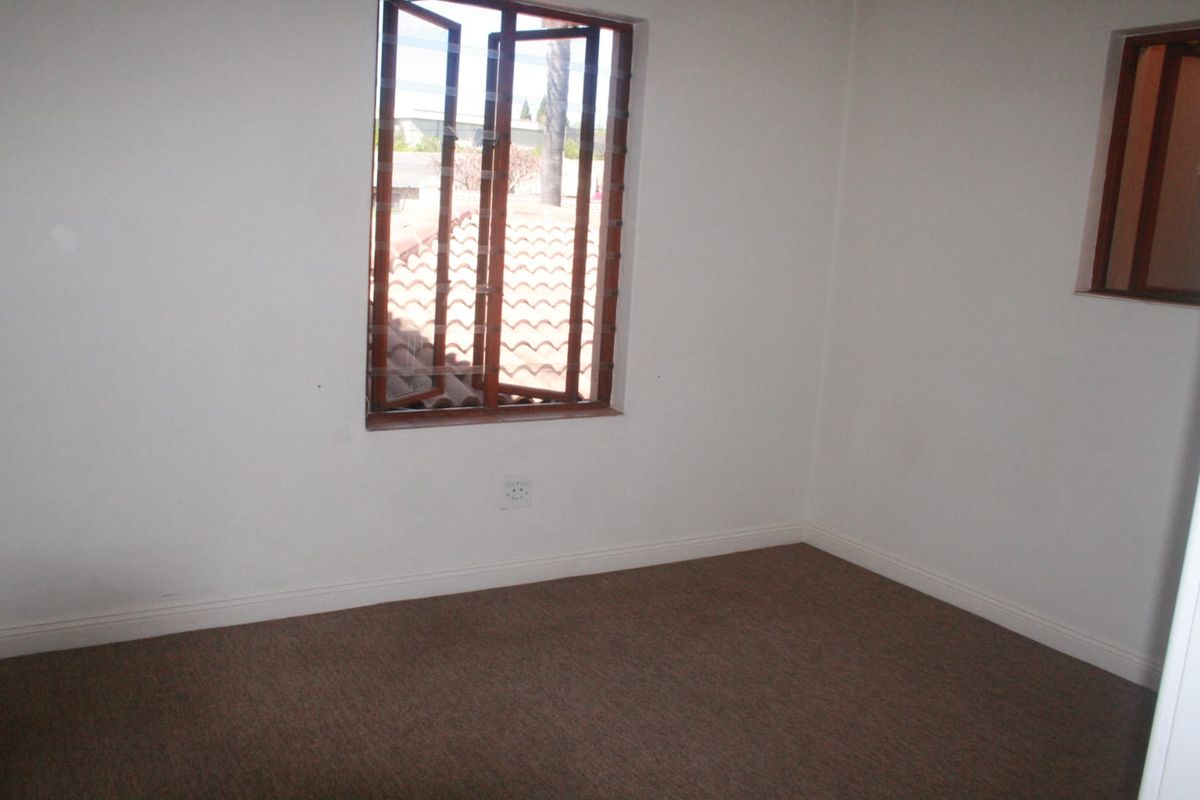 An empty bedroom featuring carpeted flooring, neutral walls, and a timber-framed casement window providing natural light.