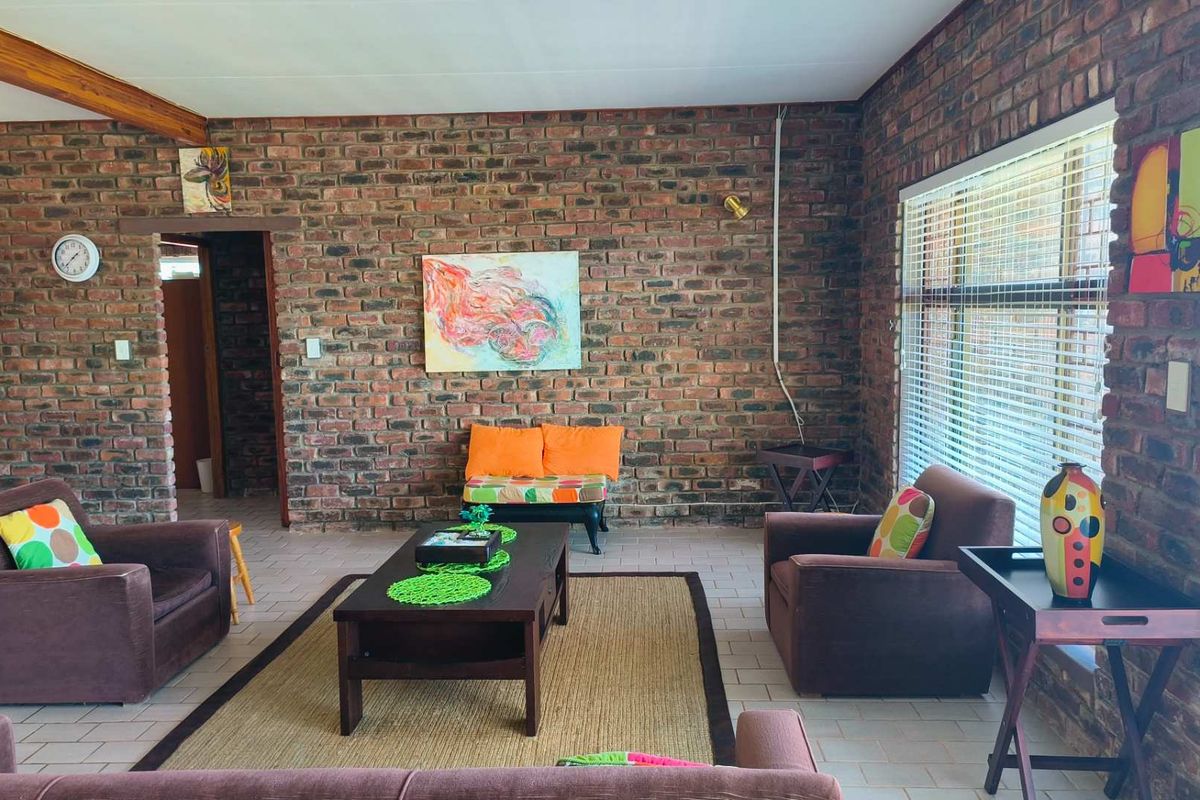 Spacious living room featuring exposed face-brick walls, tiled flooring, and large windows with fitted blinds.