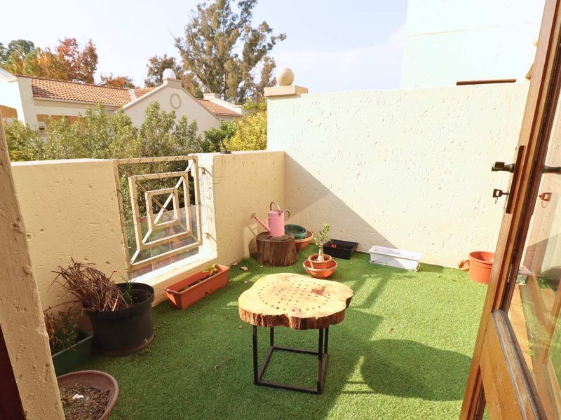 A compact, private balcony featuring artificial grass flooring, a decorative metal balustrade, and plastered boundary walls, accessible via double doors.