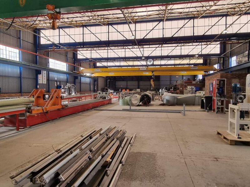 Spacious industrial warehouse featuring high ceilings, overhead gantry cranes, and concrete flooring, suitable for manufacturing or large-scale storage operations.