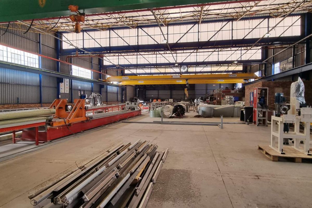 Spacious industrial warehouse featuring high ceilings, overhead gantry cranes, and concrete flooring, suitable for manufacturing or large-scale storage operations.