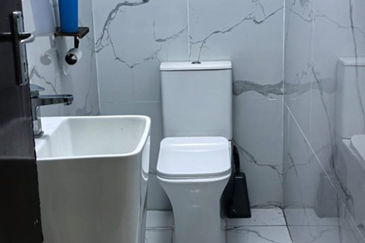 A modern, compact bathroom featuring floor-to-ceiling marble-look porcelain tiles, a sleek pedestal basin, and a contemporary toilet.