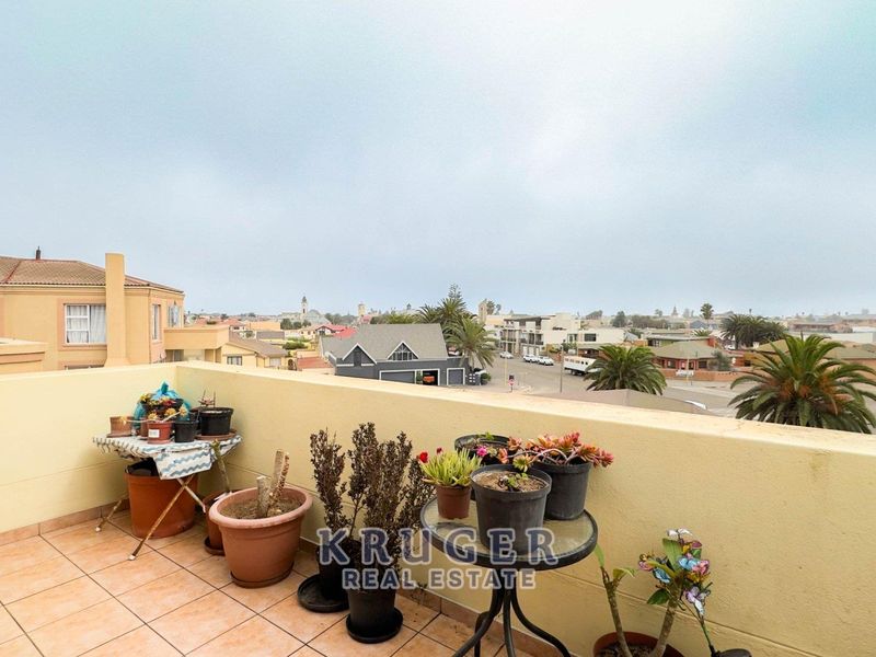 An open-air balcony featuring tiled flooring and a masonry balustrade, offering elevated views of the surrounding neighborhood.