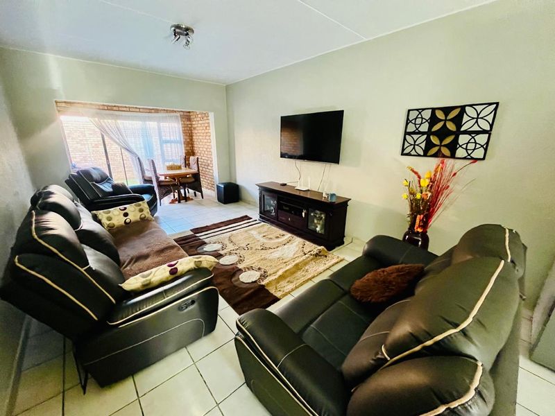 A comfortable living room featuring tiled flooring and a sliding glass door leading to an enclosed patio area with exposed brick walls.