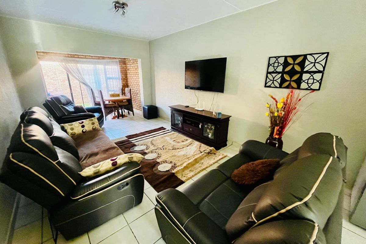 A comfortable living room featuring tiled flooring and a sliding glass door leading to an enclosed patio area with exposed brick walls.