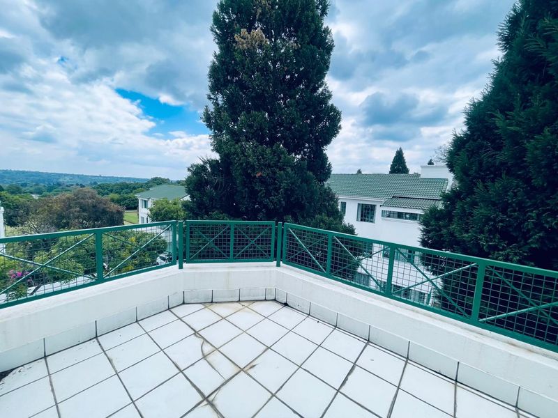 A spacious balcony featuring tiled flooring and a green metal balustrade, offering elevated views of the surrounding landscape and neighboring properties.