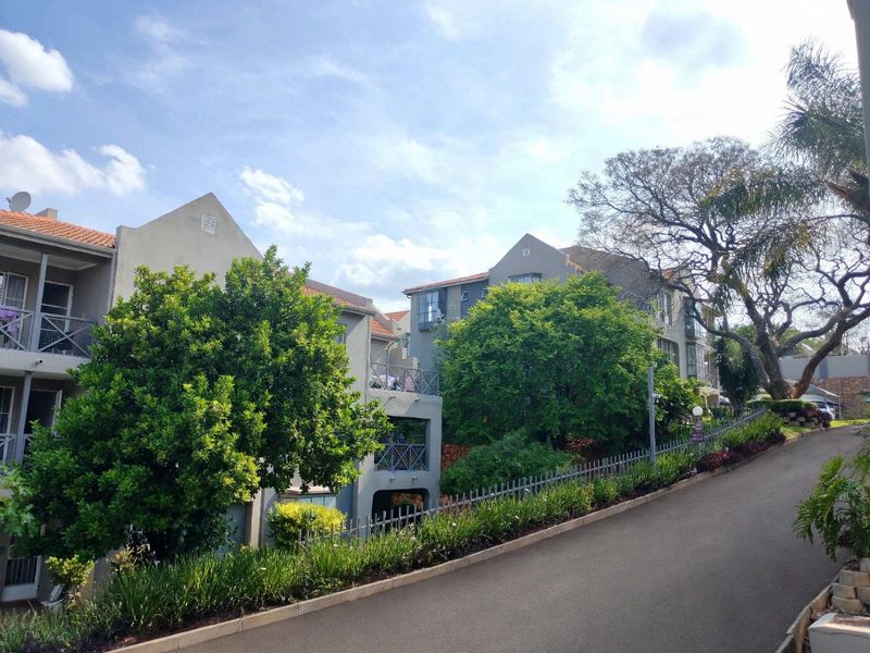 Exterior view of a multi-story townhouse complex featuring tiled roofs, private balconies with metal railings, and a paved driveway approach.