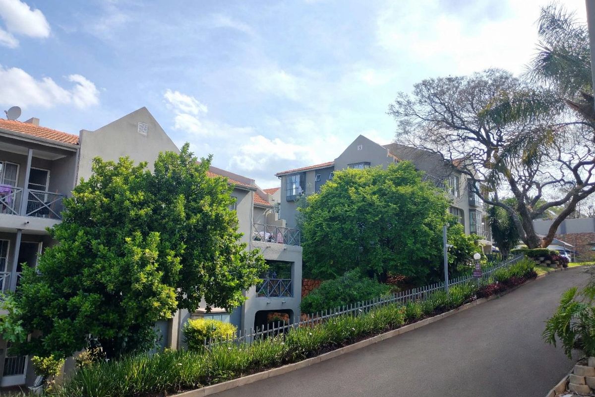 Exterior view of a multi-story townhouse complex featuring tiled roofs, private balconies with metal railings, and a paved driveway approach.