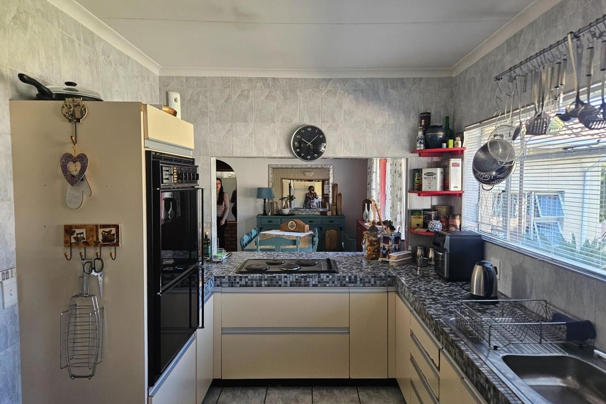 A functional kitchen featuring built-in cabinetry, a wall-mounted oven, a hob, and a stainless steel sink with a view into the adjacent dining area.