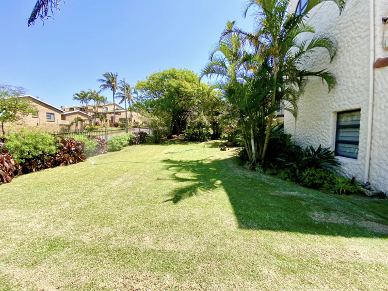 A well-maintained garden area featuring a lush lawn, mature palm trees, and textured exterior wall cladding with louvre windows.