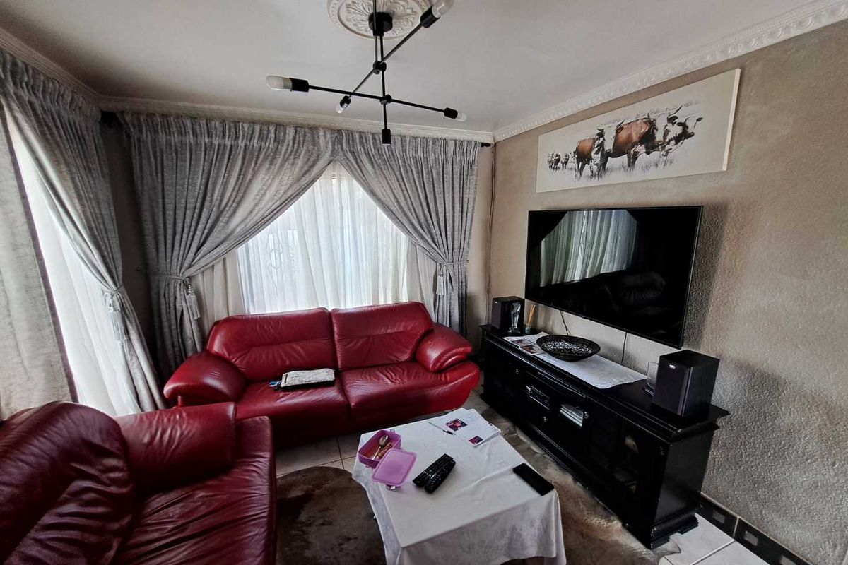 A cozy living room featuring tiled flooring, coved cornicing, and a decorative ceiling rose with a modern light fixture.