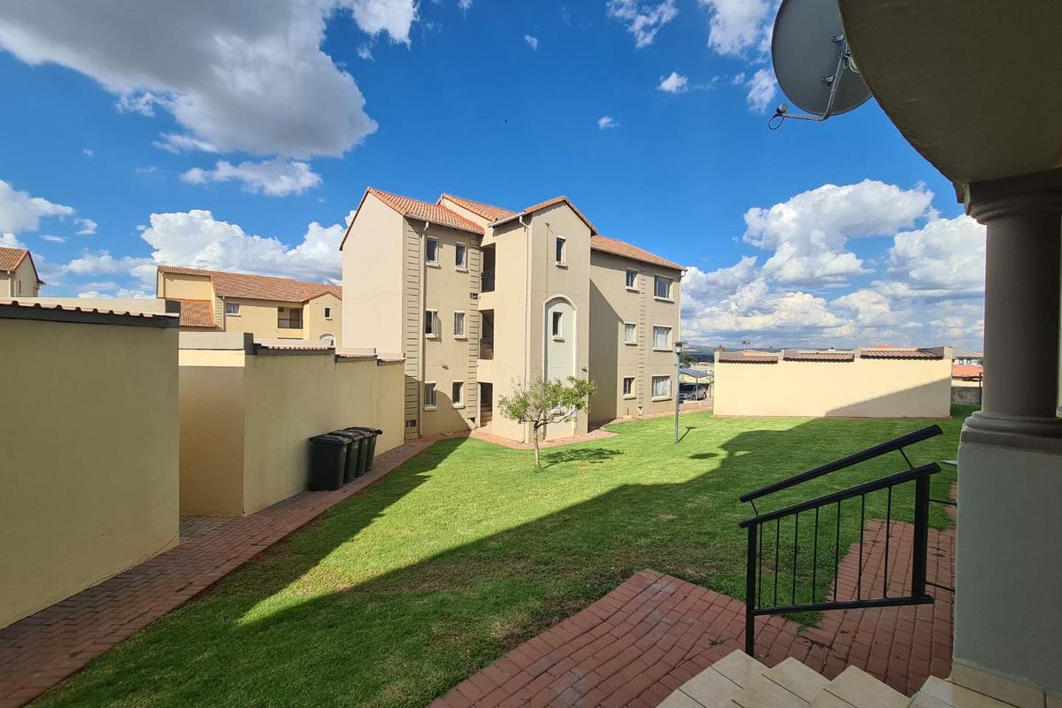 View of the apartment complex rear exterior, featuring a communal lawn, brick paved pathways, and boundary walls.