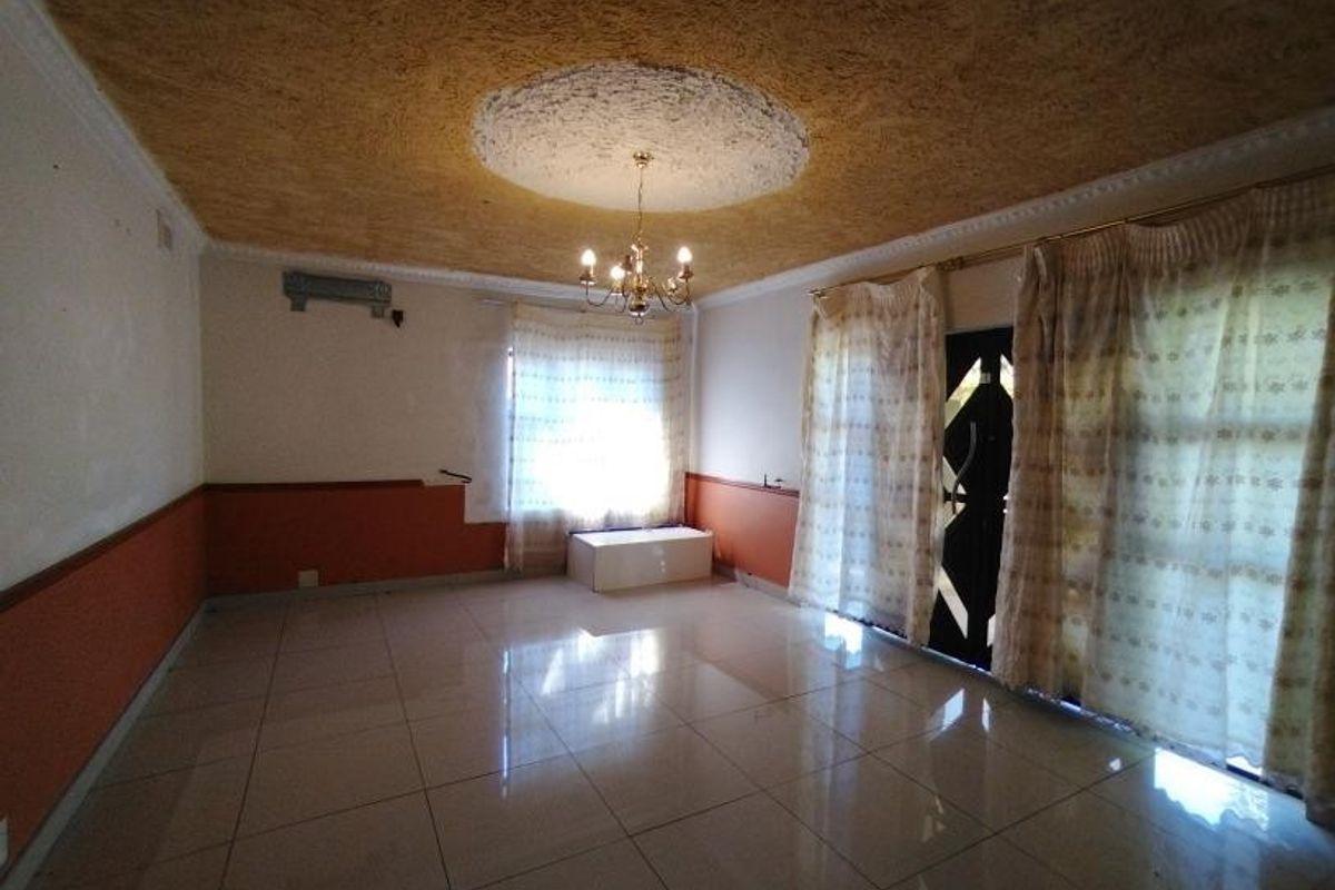 Spacious living room featuring large floor tiles, a textured ceiling with a central chandelier, and sliding glass doors leading to the exterior.