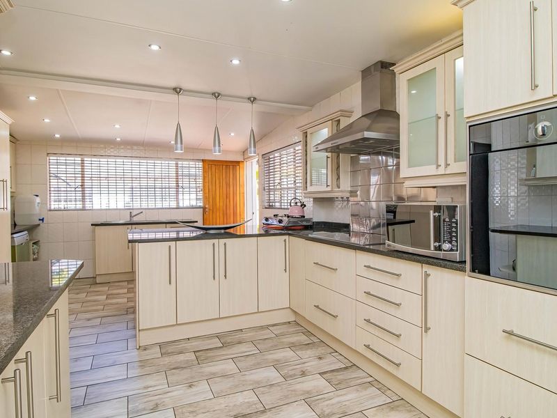 A well-maintained kitchen featuring light wood-finish cabinetry, granite countertops, integrated stainless steel appliances, and modern tiled flooring with ample natural light.