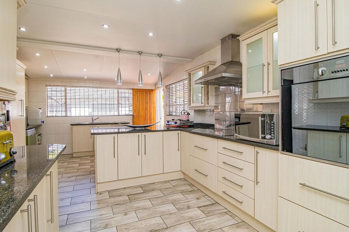 A well-maintained kitchen featuring light wood-finish cabinetry, granite countertops, integrated stainless steel appliances, and modern tiled flooring with ample natural light.