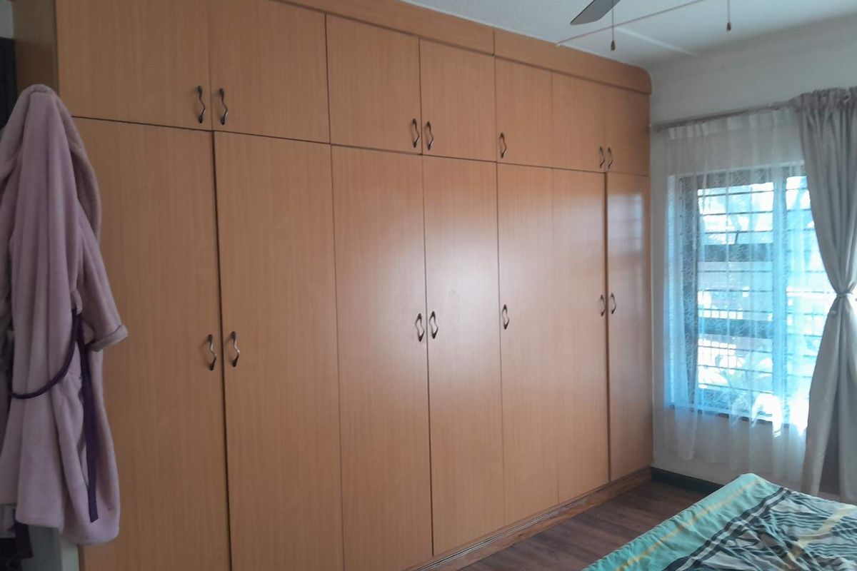 Bedroom featuring extensive floor-to-ceiling built-in wooden cupboards, a ceiling fan, and a window with security bars.