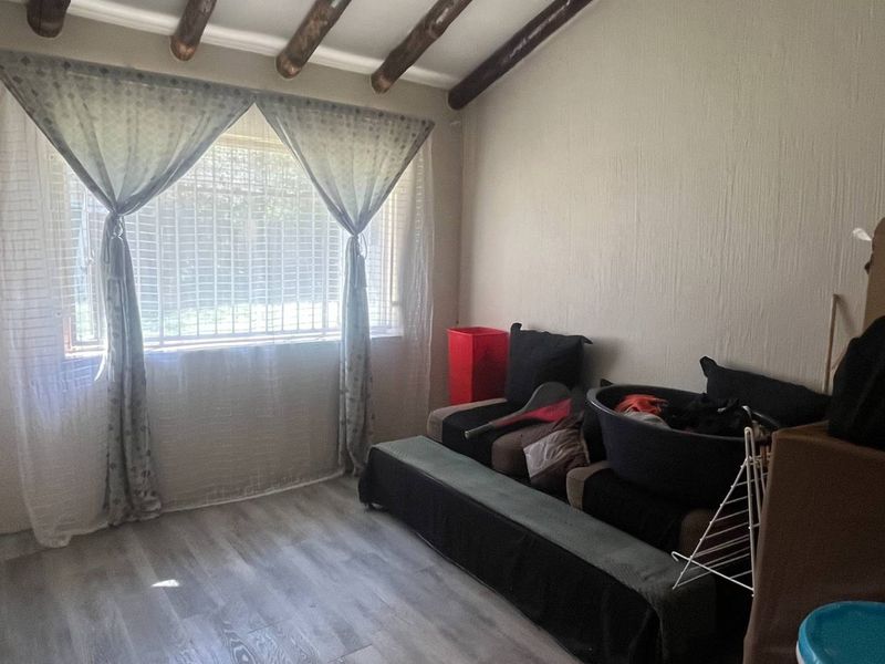 A bedroom featuring exposed timber ceiling beams, laminate flooring, and a window fitted with security bars.