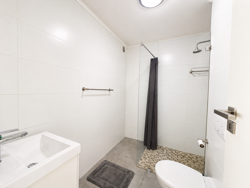 A clean, modern bathroom featuring white wall tiles, a glass shower screen, a wall-mounted basin, and a toilet with neutral floor tiling.