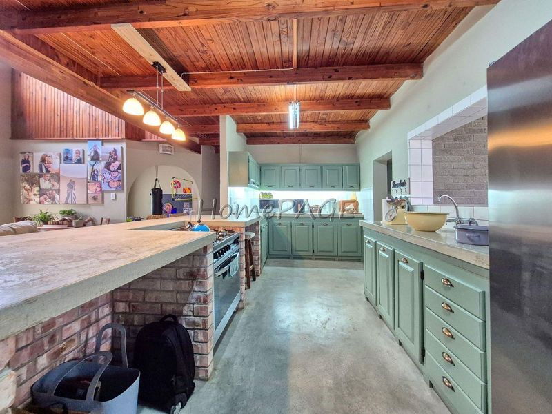 Spacious kitchen featuring exposed timber beam ceilings, concrete countertops, a brick island with a built-in gas stove, and ample fitted cabinetry.