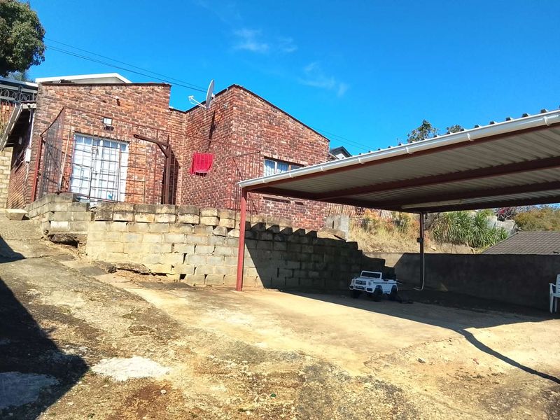 Front exterior view of a face brick house featuring a covered carport, concrete driveway, and a retaining wall structure.