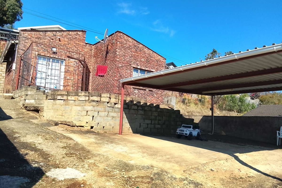 Front exterior view of a face brick house featuring a covered carport, concrete driveway, and a retaining wall structure.