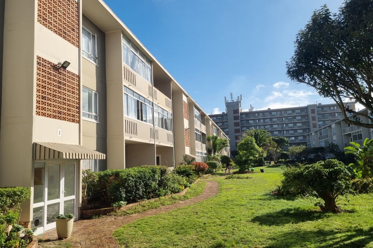 A view of the apartment building exterior featuring a well-maintained garden, brick pathways, and architectural breeze block detailing.