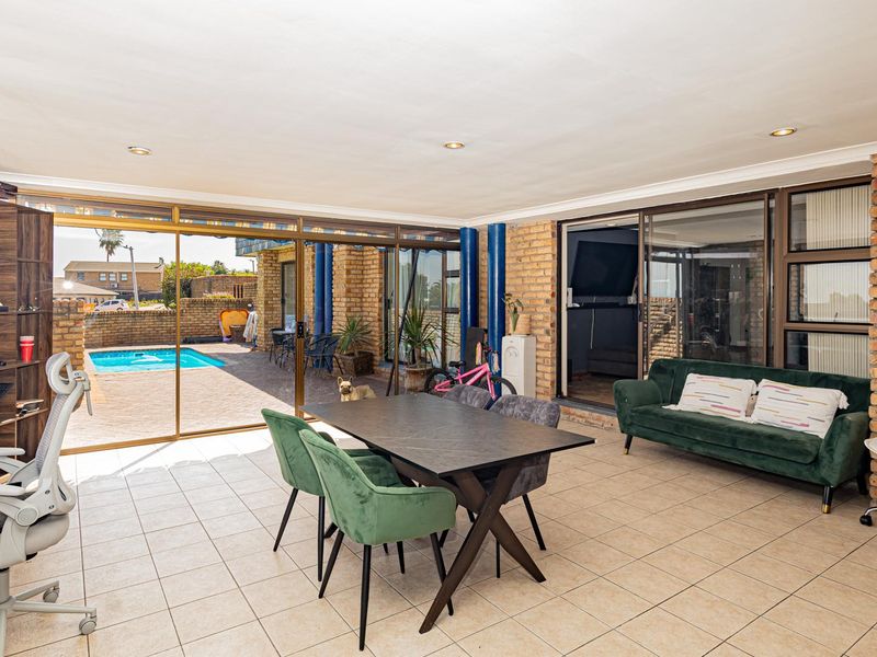 Spacious open-plan living area featuring tiled floors, exposed brick walls, and large sliding glass doors providing seamless access to the outdoor pool area.