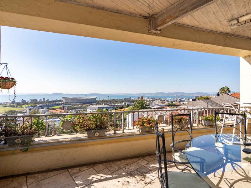 A covered balcony featuring stone flooring, a timber ceiling, and a metal balustrade, offering expansive panoramic views of the city and coastline.