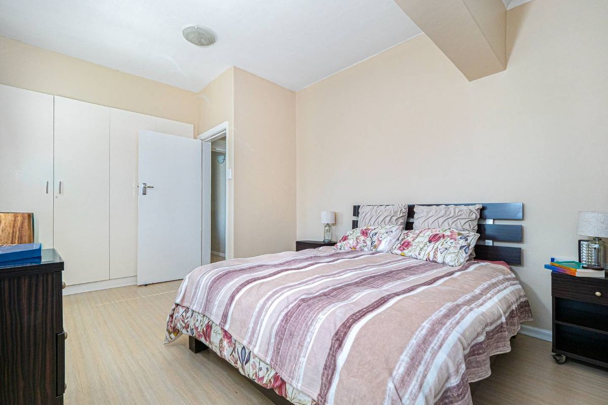 A well-lit bedroom featuring built-in floor-to-ceiling wardrobes, light wood-look flooring, and neutral wall tones.