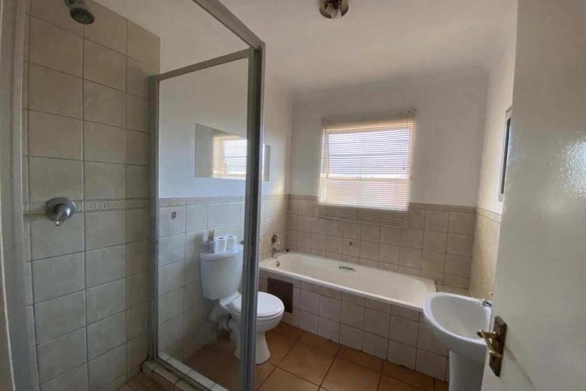 A functional bathroom featuring a separate shower enclosure, a standard bathtub, a pedestal basin, and neutral wall tiling.