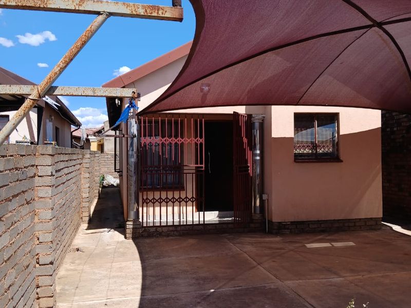 Rear exterior area featuring a paved courtyard, brick boundary wall, and a large shade sail structure with visible rust on the metal supports.