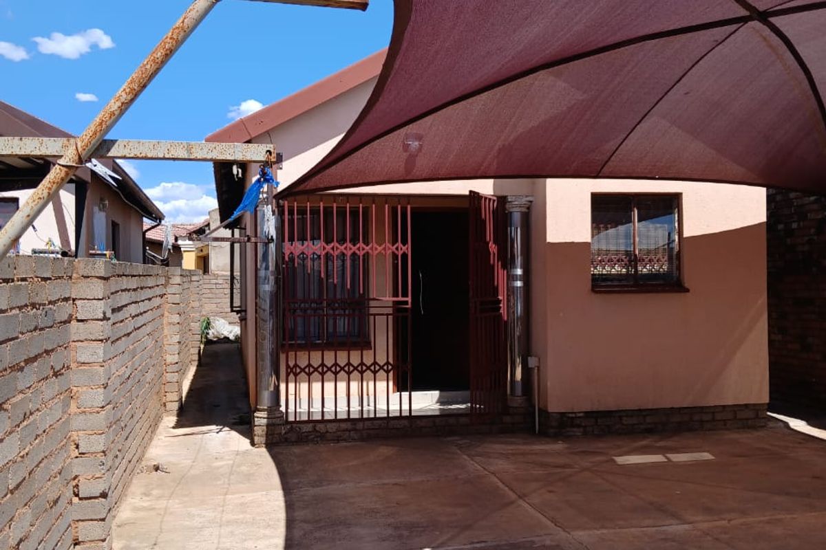 Rear exterior area featuring a paved courtyard, brick boundary wall, and a large shade sail structure with visible rust on the metal supports.