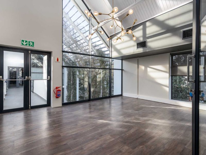 Spacious, light-filled office area featuring high vaulted ceilings, expansive floor-to-ceiling glass windows, and modern laminate flooring in a professional business setting.