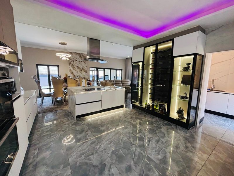 Modern open-plan kitchen featuring a central island, built-in appliances, integrated wine display cabinetry, and sophisticated recessed ceiling lighting with polished tiled flooring.