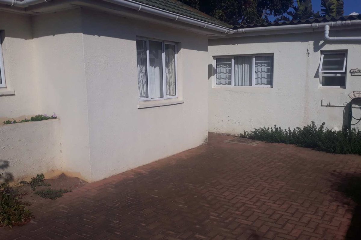 A rear exterior view of the property featuring a paved courtyard area, white rendered walls, and security-fitted windows.