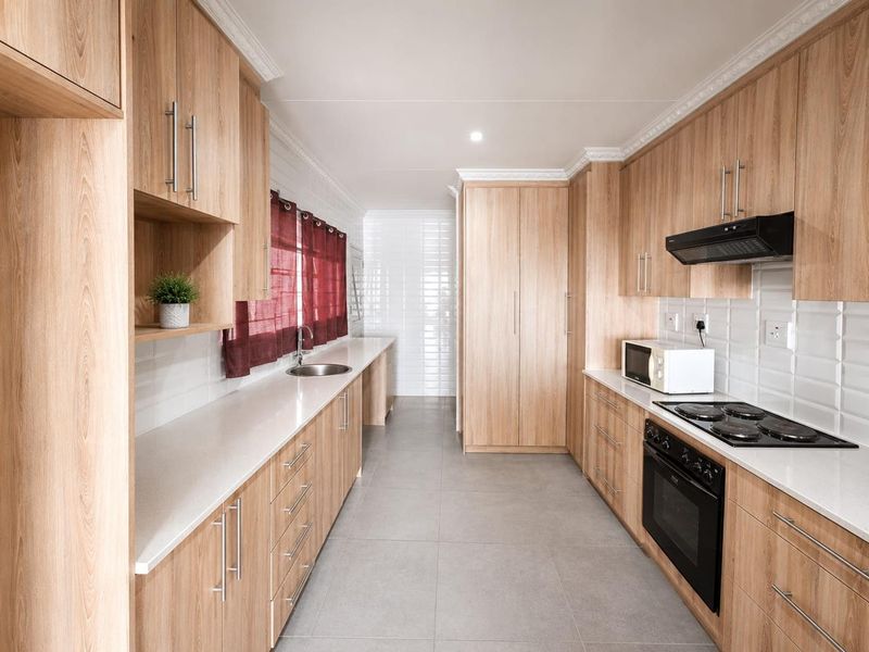 Modern galley-style kitchen featuring light wood cabinetry, stone countertops, integrated oven, electric hob, extractor fan, and sleek tiled finishes.
