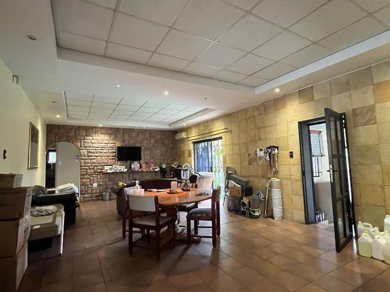 Spacious open-plan living and dining area featuring a stone feature wall, tiled flooring, and a suspended ceiling with recessed lighting.