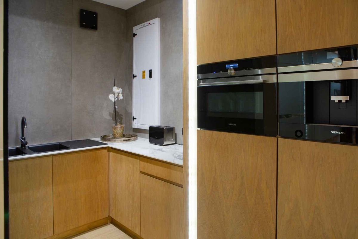 Modern kitchenette featuring wood-veneer cabinetry, marble-effect countertops, integrated Siemens oven and coffee machine, and a sleek black sink.