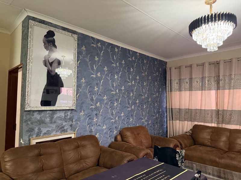 A living room featuring decorative patterned wallpaper, a prominent crystal chandelier, and classic cove cornicing, providing a traditional aesthetic foundation.