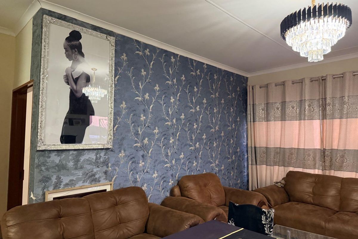A living room featuring decorative patterned wallpaper, a prominent crystal chandelier, and classic cove cornicing, providing a traditional aesthetic foundation.
