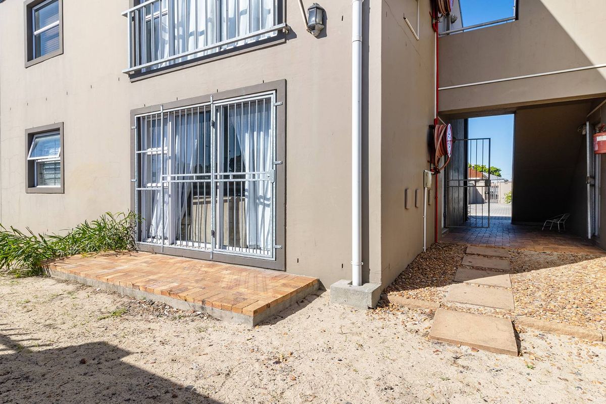 Rear exterior view of the apartment building featuring a small brick paved patio, security bars on windows, and communal access walkway.