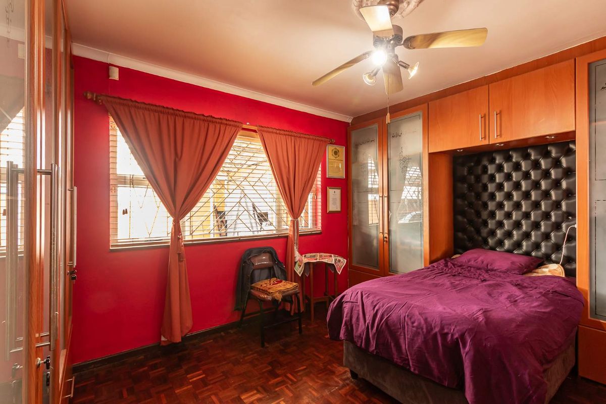 A bedroom featuring parquet flooring, built-in wooden cupboards with glass detailing, and a ceiling fan.