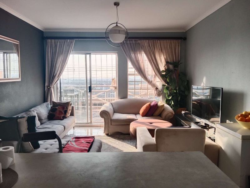 A comfortable living room featuring tiled floors, a central pendant light, and large sliding glass doors that provide access to an outdoor balcony area.
