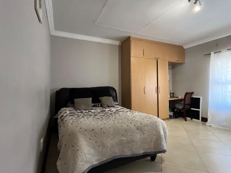 A bedroom featuring tiled flooring, ceiling cornice, and a built-in wardrobe with an integrated desk space.