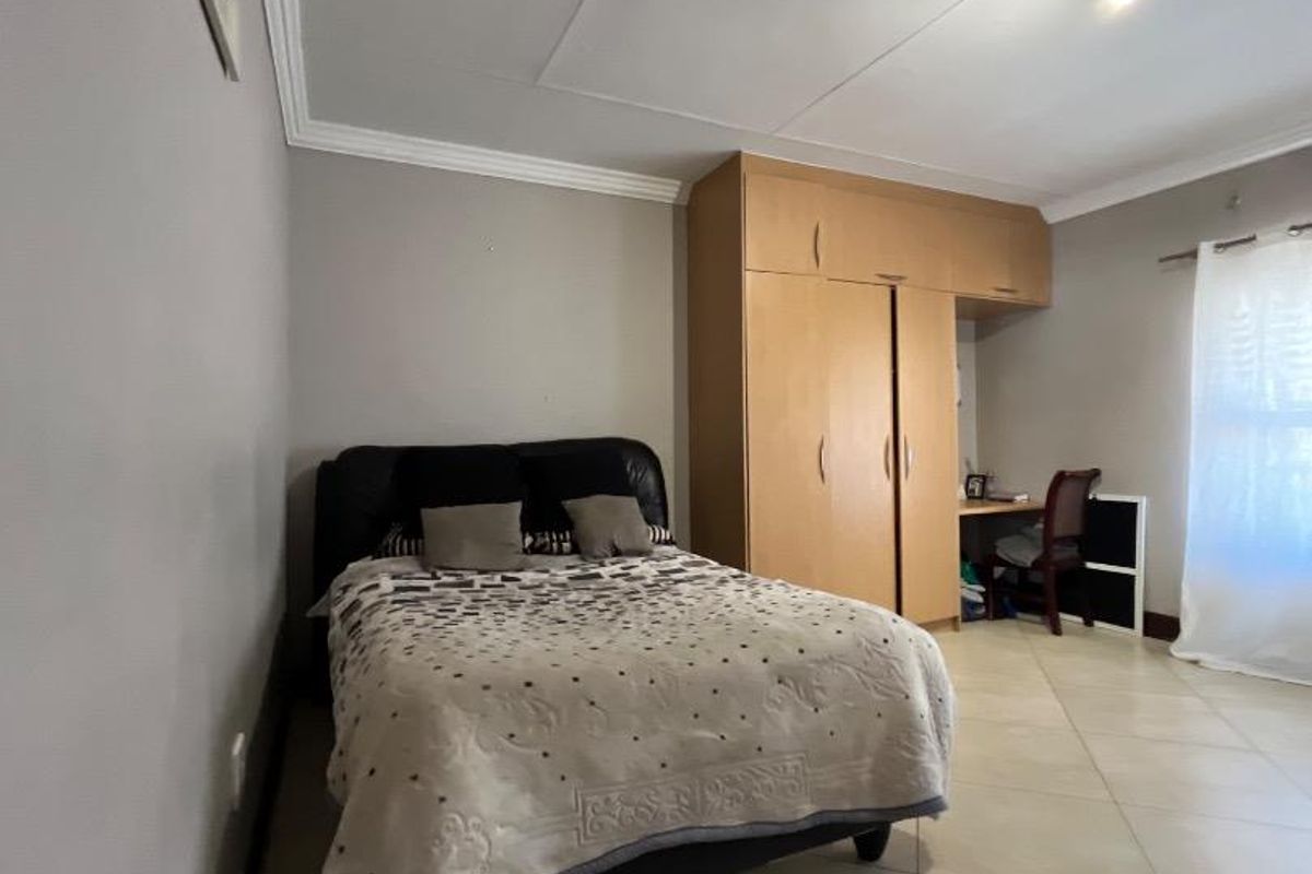 A bedroom featuring tiled flooring, ceiling cornice, and a built-in wardrobe with an integrated desk space.