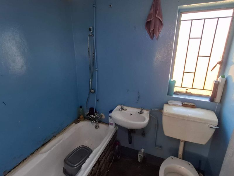 A compact bathroom featuring a bathtub, pedestal basin, and toilet, requiring cosmetic updates to improve the overall condition and aesthetic appeal.